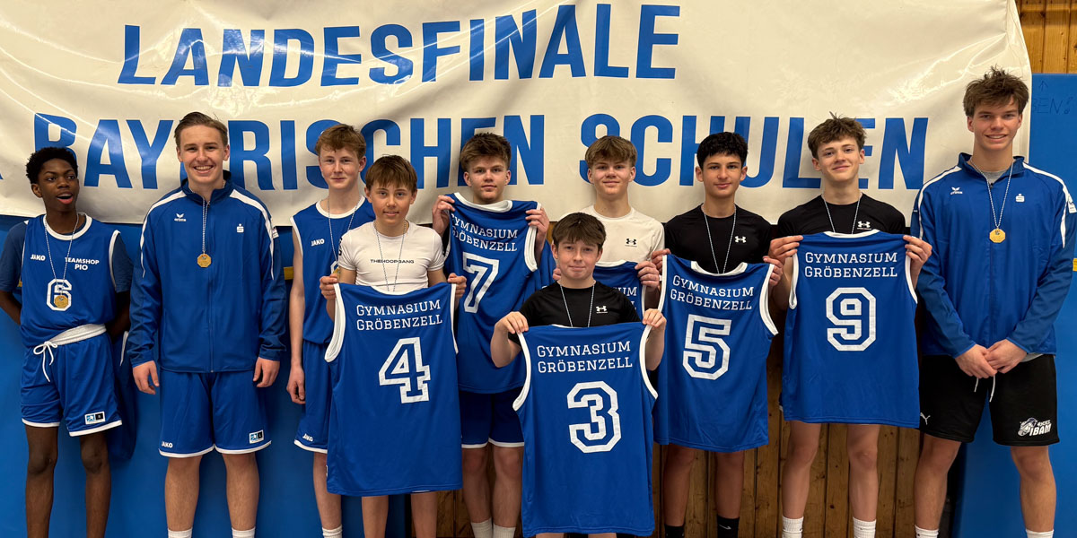 IMG_7687-2-2 Eine Gruppe von zehn Jungen in einheitlichen Sportuniformen steht vor einem Banner mit der Aufschrift „Landesfinale Bayerischen Schulen“. Sie halten Basketballtrikots mit der Aufschrift „Gymnasium Gröbenzell“, lächeln und tragen Medaillen.
